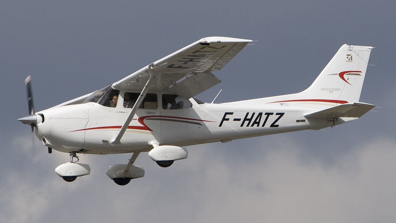 A 2018 Cessna 172S Skyhawk SP (F-HATZ) in flight, photographed from below against an overcast sky